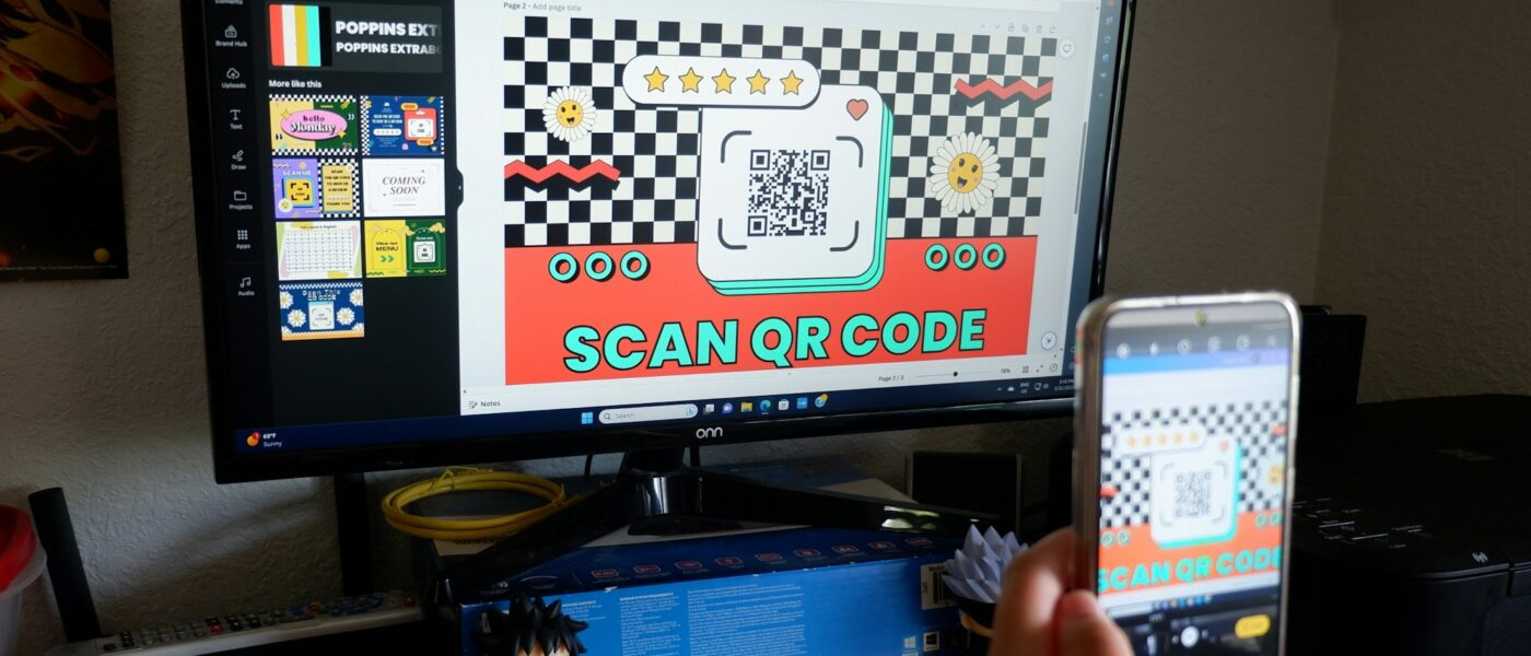 Seseorang memegang ponsel di depan layar komputer untuk memindai kode QR