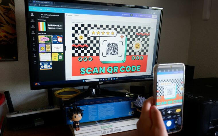 Seseorang memegang ponsel di depan layar komputer untuk memindai kode QR